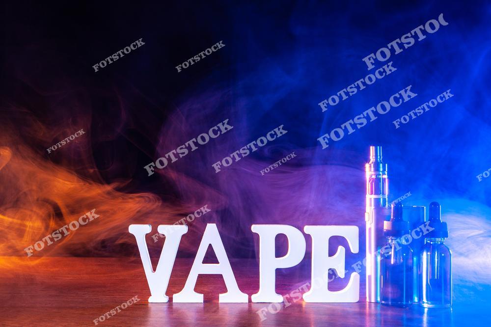 Стильное изображение популярного vape-мода и электронной сигареты на столе в облаках густого пара. На фотографии представлены современные устройства для вейпинга, жидкости для электронных сигарет и аксессуары для парения, создающие атмосферу современной vape-культуры и технологичного lifestyle. Дым от вейпа и минималистичная композиция делают изображение идеальным для рекламы vape shop, интернет-магазинов электронных сигарет и товаров для вейперов. Фотография отлично подходит для маркетинговых материалов, баннеров, каталогов продукции и публикаций о современных устройствах для альтернативного курения.